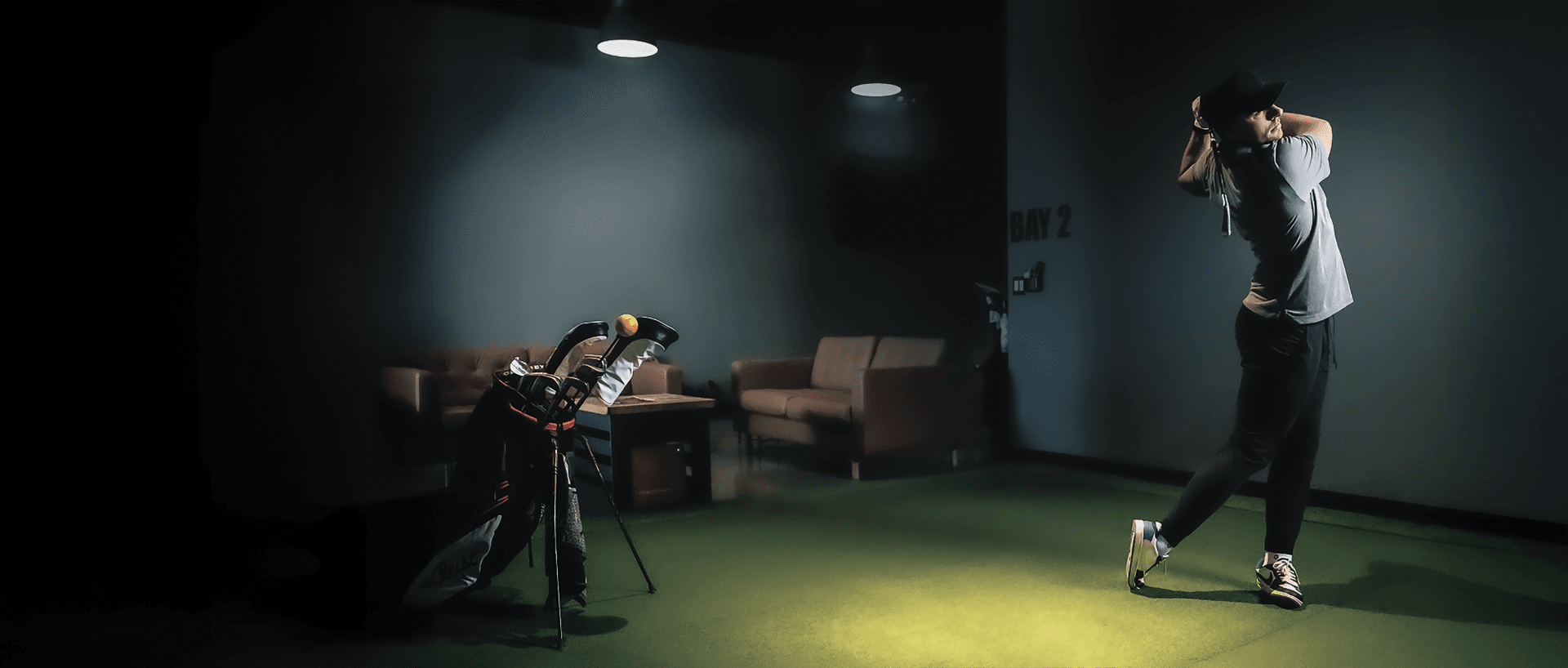A golfer mid-swing in a Back Nine simulator bay
